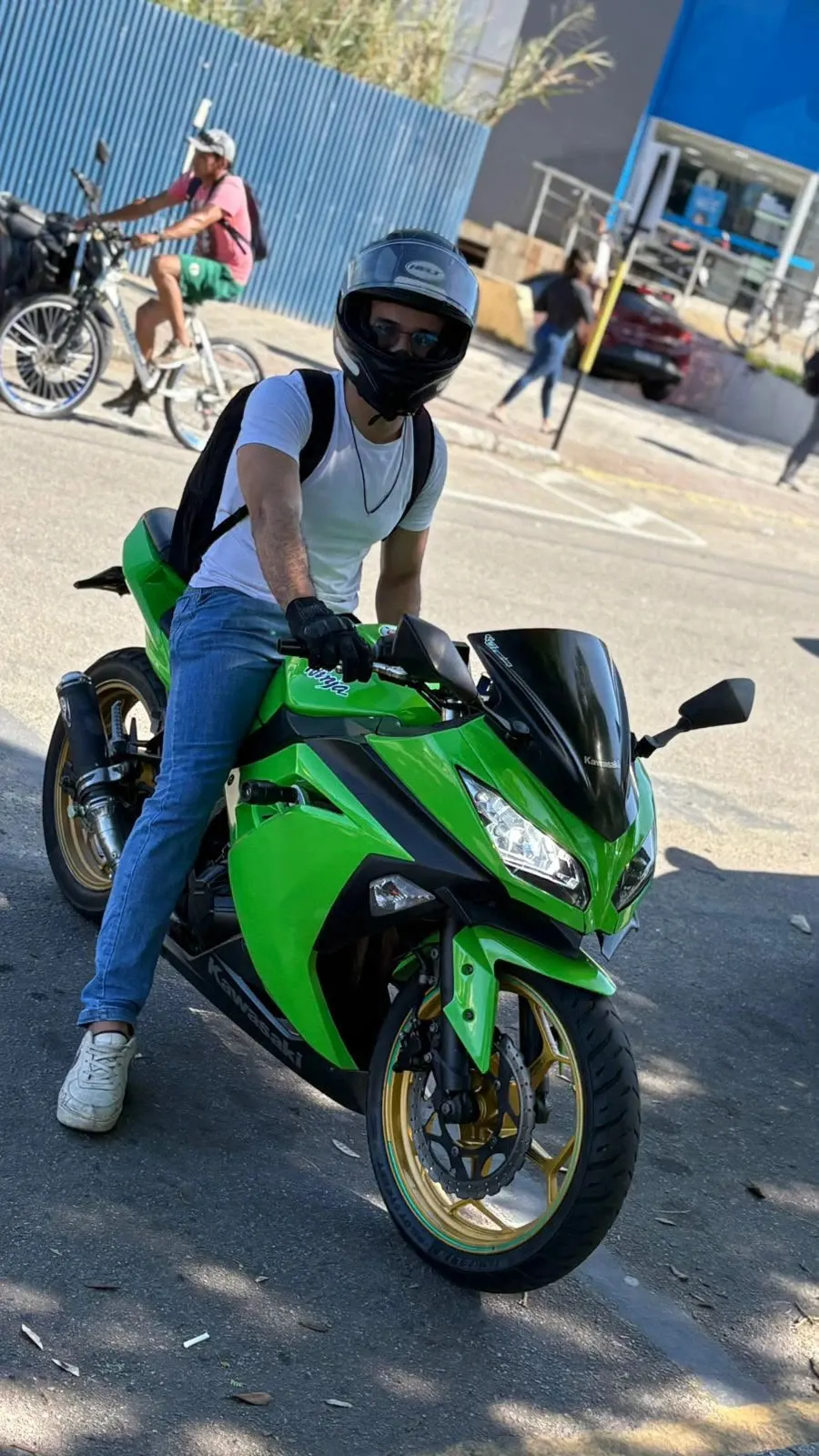 José, de capacete, sentado na Kawasaki Ninja 300 verde, parado na rua